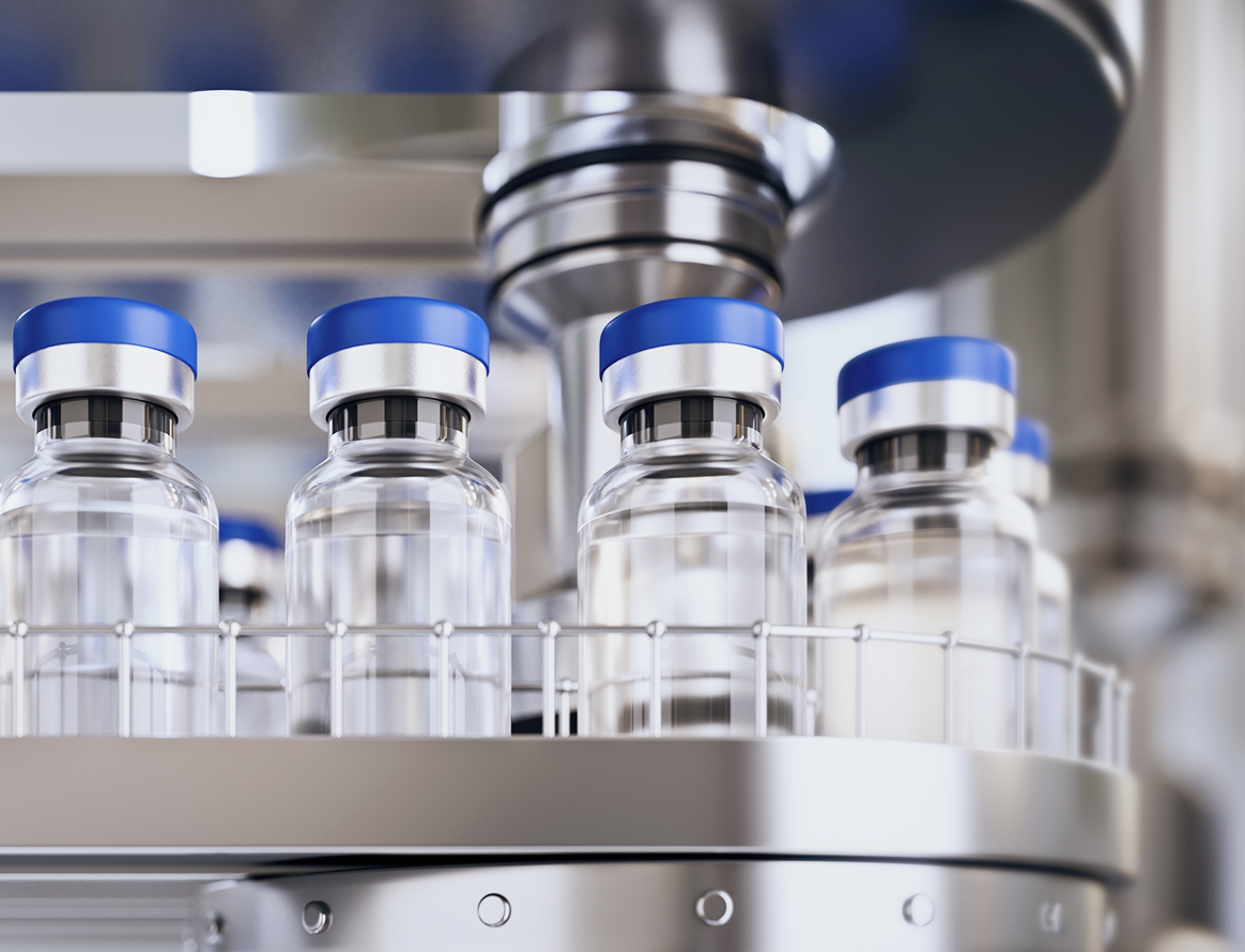 A close-up of several medical vials with blue caps moving along an automated pharmaceutical production line.
